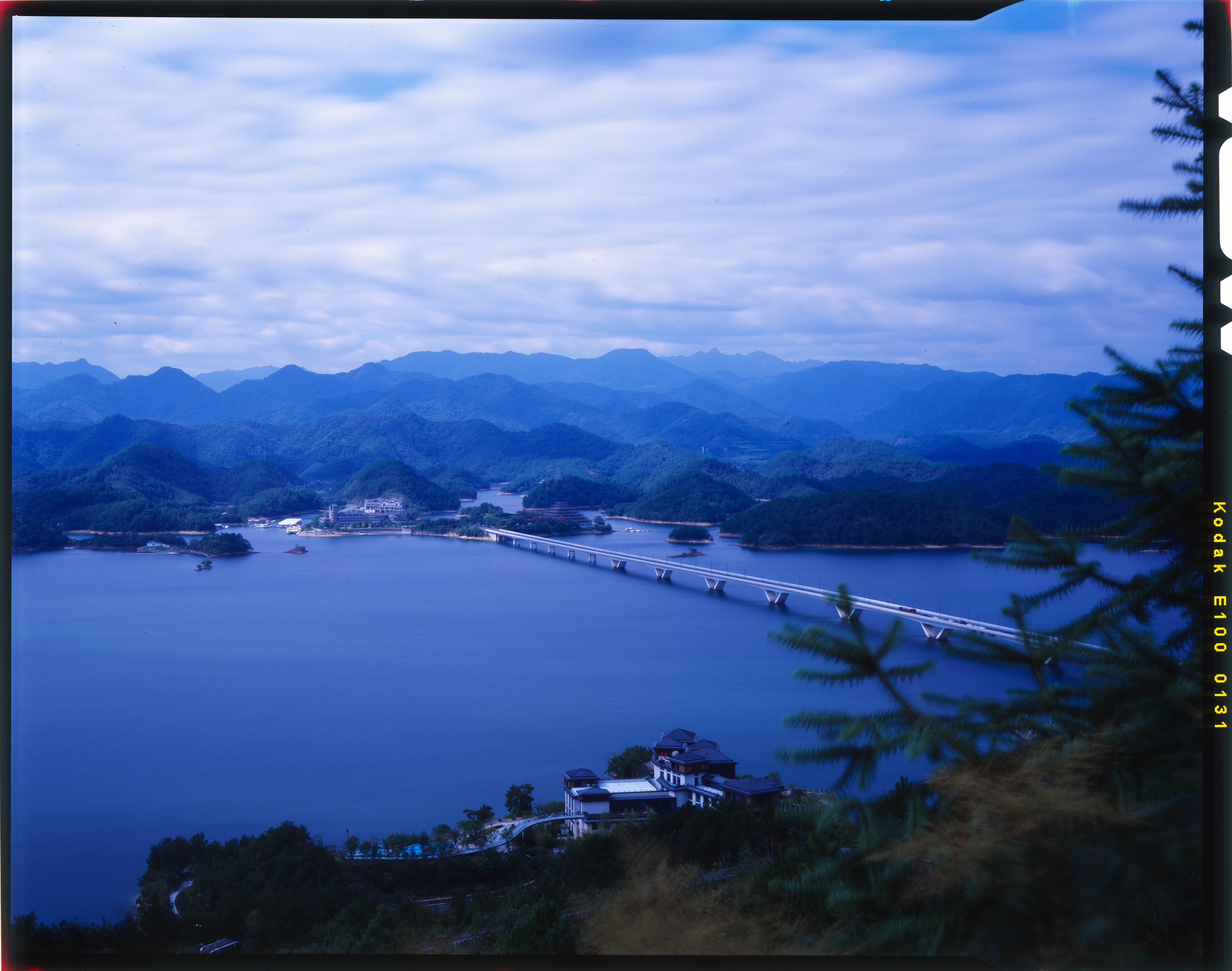 层叠群山环抱湖面，一座长桥伸向远处，完整保留胶片片边。