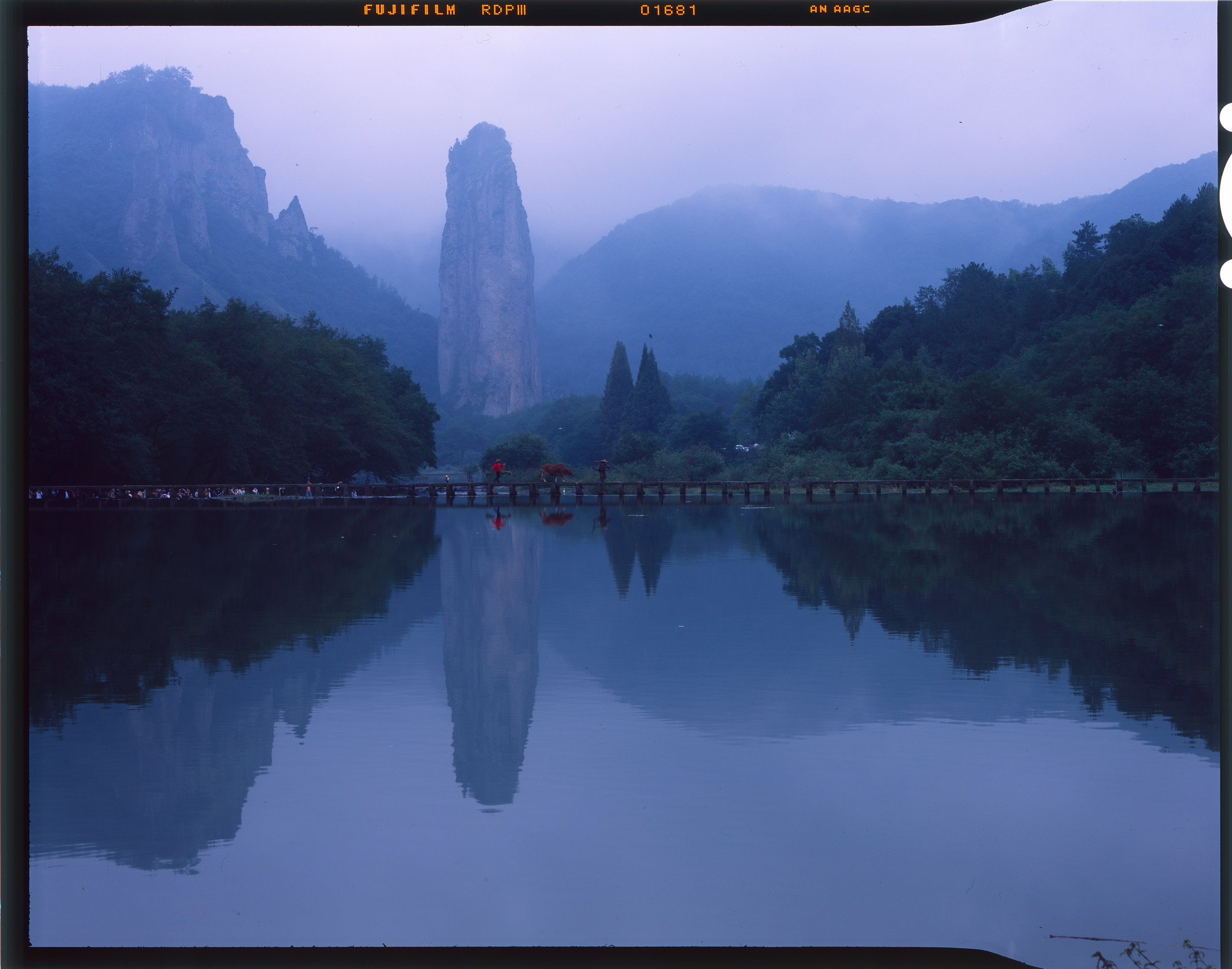 云雾笼罩石峰与树林，倒影落在静水中，完整保留胶片片边。